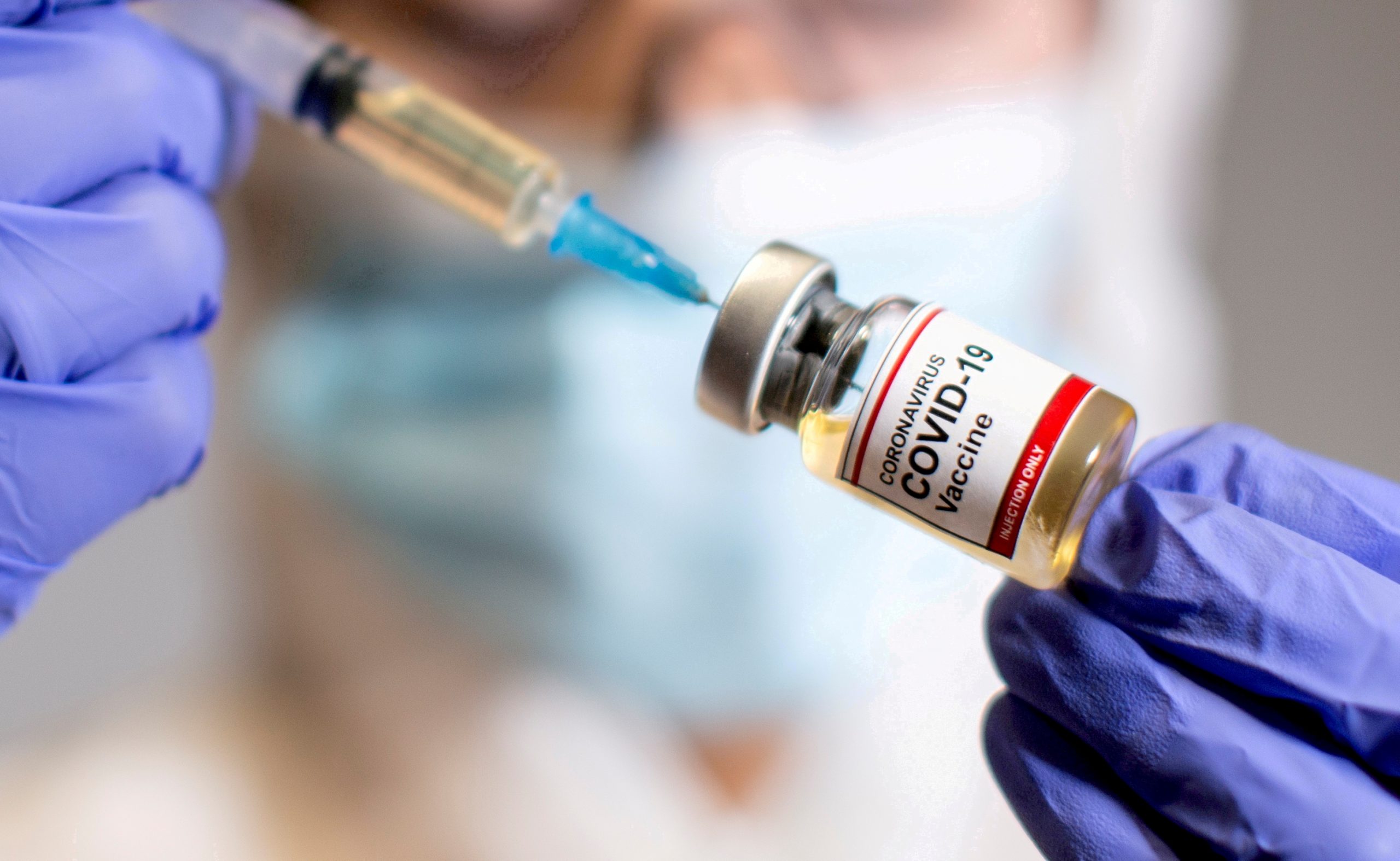 A woman holds a medical syringe and a small bottle labelled "Coronavirus COVID-19 Vaccine